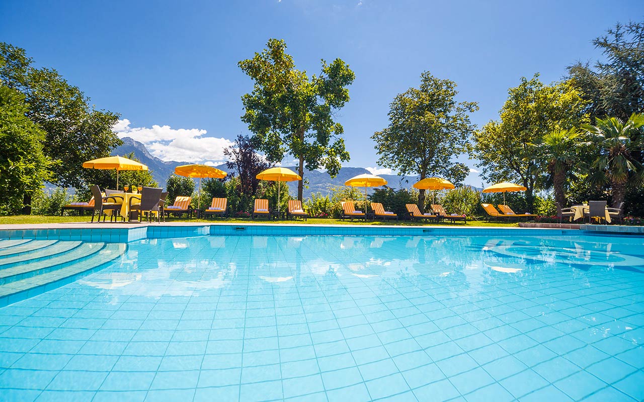 Outdoor pool with beach umbrellas and deck chairs at the hotel Kristall in Marling in a sunny day