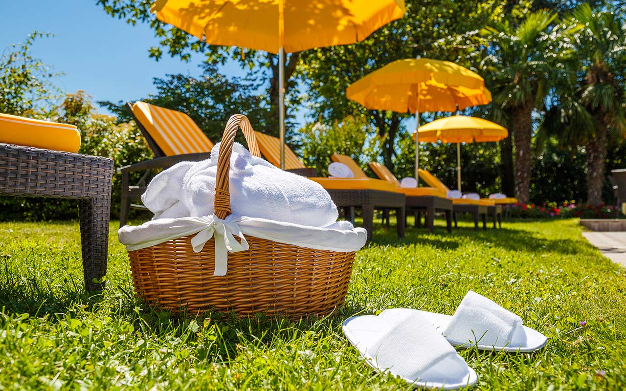 Korb mit Badetüchern und Badeslippers im Garten mit Liegestühlen und Sonnenschirmen im Hotel Kristall