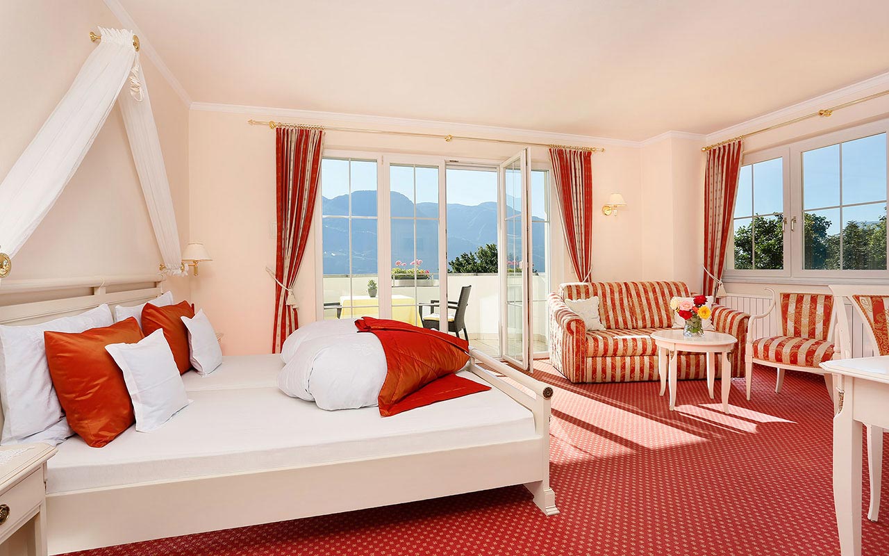 Luminosa camera matrimoniale con moquette rossa, balcone e finestra all'Hotel Kristall vicino Merano