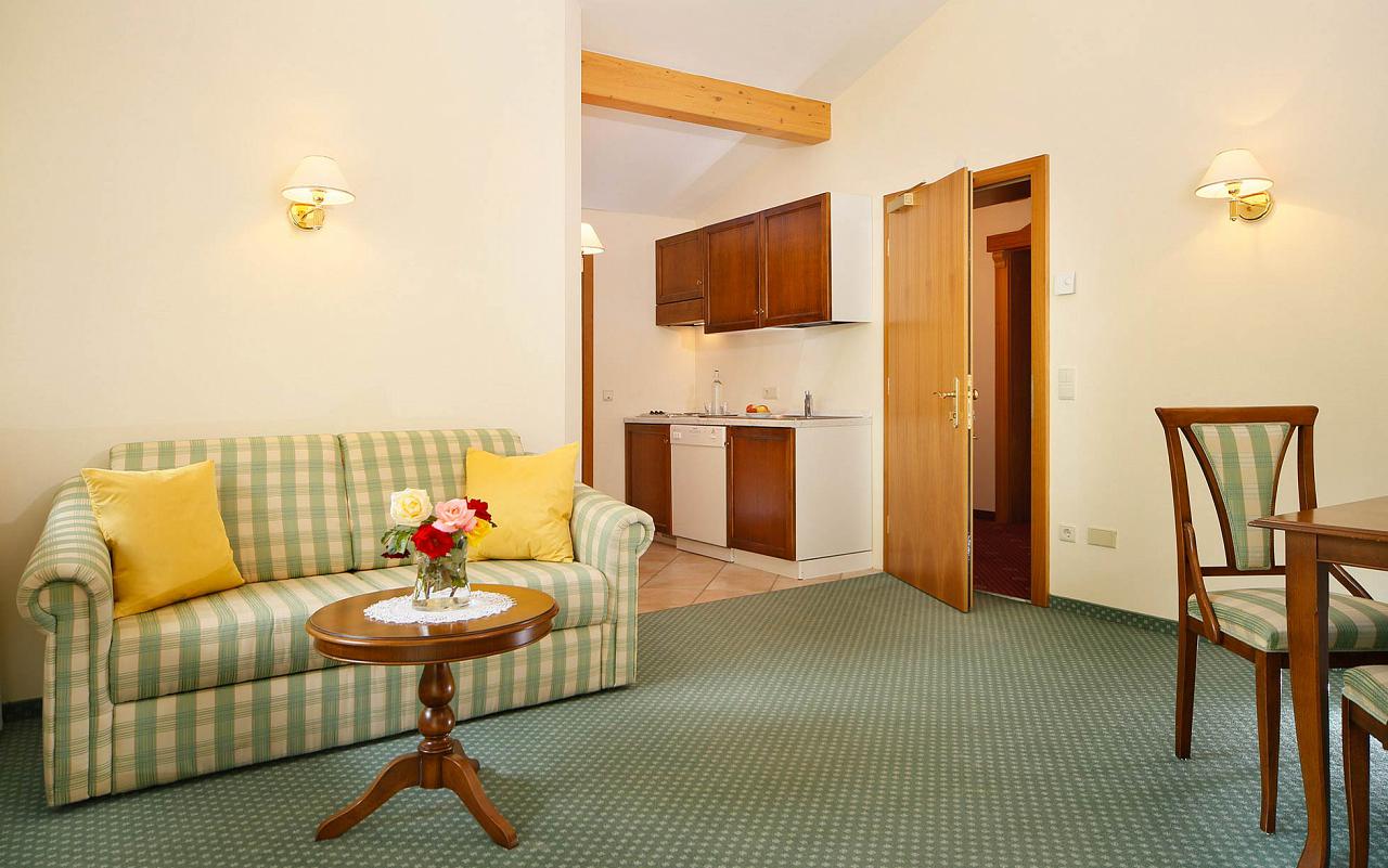 Interno di un appartamento all'Hotel Kristall: divanetto e tavolino in primo piano e cucinino sullo sfondo