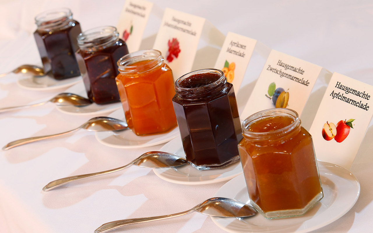 Cinque barattoli di diverse marmellate con cucchiaini per servirsi