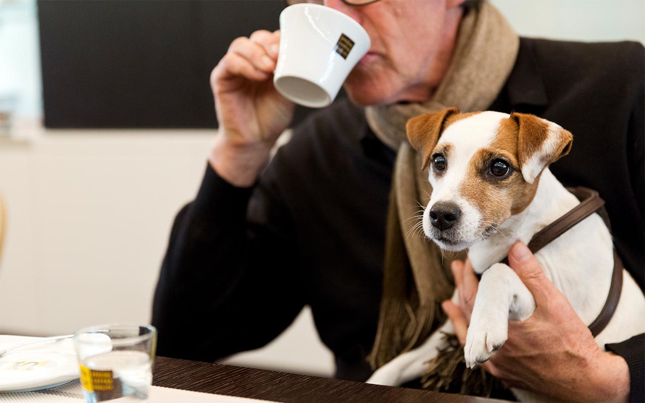 Signore anziano che sorseggia un caffè e tiene in braccio un jack russell