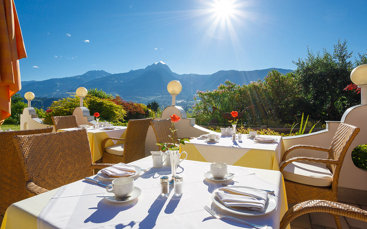 Gedeckte Tische auf der Sonnenterrasse des Hotels Kristall mit Blick auf das Meraner Land