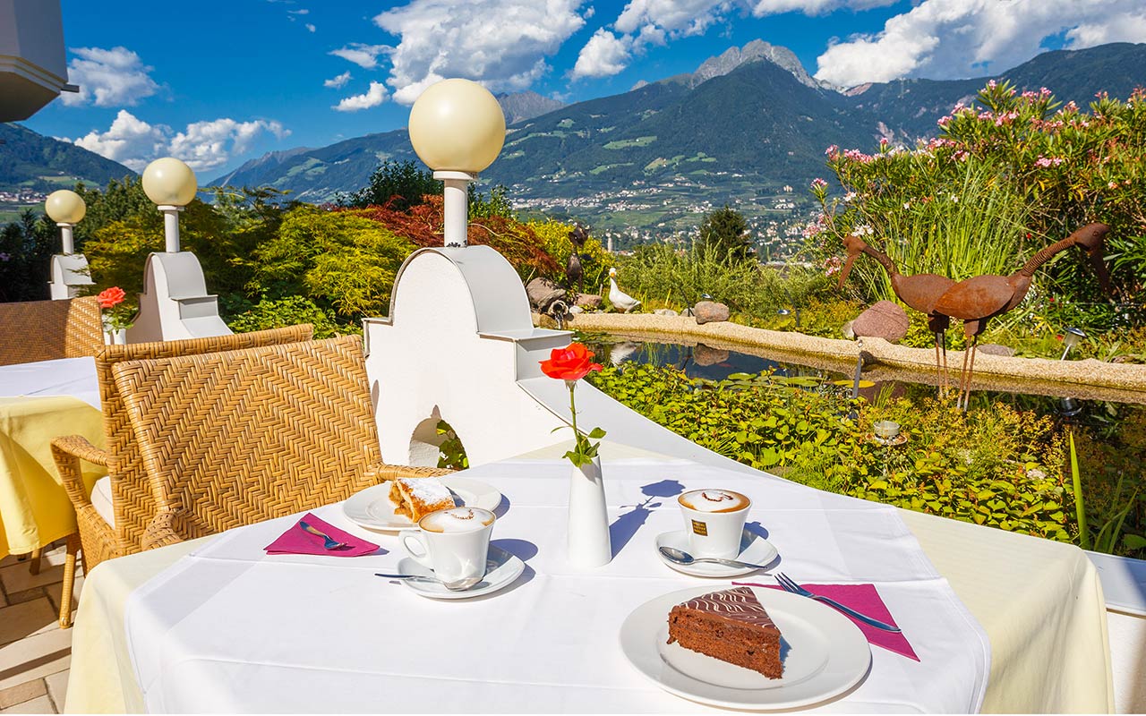 Primo piano di un tavolino apparecchiato con due fette di torta nella veranda all'aperto dell'hotel Kristall a Marlengo